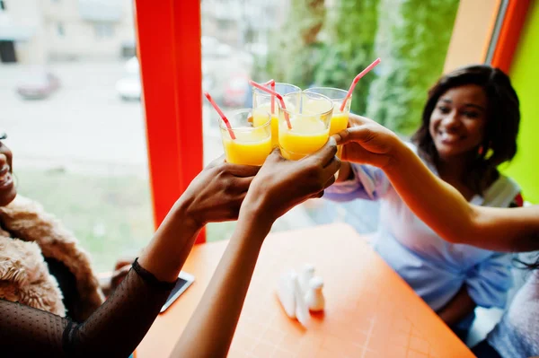 Quatro jovens meninas africanas aplaudem com sucos de laranja enquanto se sentam — Fotografia de Stock
