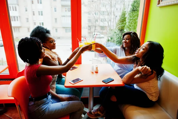 Quatro jovens meninas africanas aplaudem com sucos de laranja enquanto se sentam — Fotografia de Stock