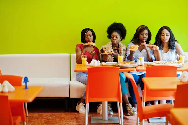 Quatro jovens meninas africanas em restaurante colorido brilhante comendo piz — Fotografia de Stock