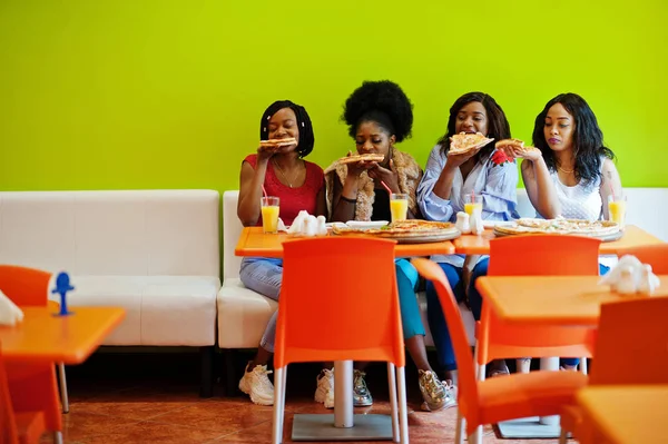 Quatro jovens meninas africanas em restaurante colorido brilhante comendo piz — Fotografia de Stock