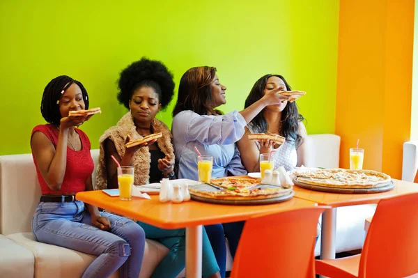 Quatro jovens meninas africanas em restaurante colorido brilhante comendo piz — Fotografia de Stock