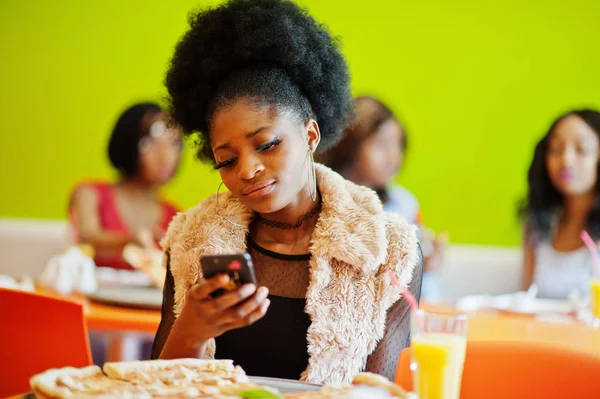 African woman with pizza sitting at restaurant with mobile phone