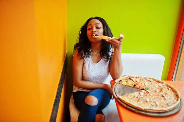 Afrykańska kobieta z pizzą siedzi w jasnej kolorowej restauracji. — Zdjęcie stockowe