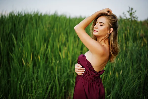 Mujer sensual rubia en vestido de marsala rojo posando en las cañas . —  Fotos de Stock