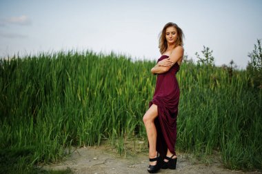 Kırmızı marsala elbiseli sarışın şehvetli kadın sazlıkpozlar poz.