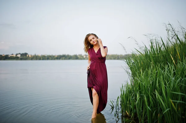Blonde femme sensuelle en robe de marsala rouge debout dans l'eau de l — Photo