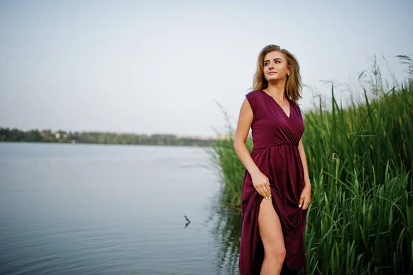 Blonde sensual woman in red marsala dress standing in water of l