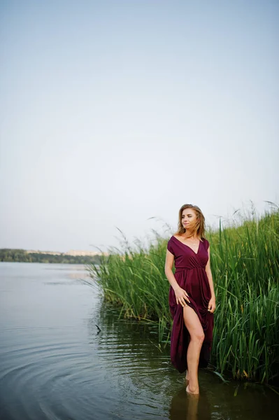 Blonde femme sensuelle en robe de marsala rouge debout dans l'eau de l — Photo