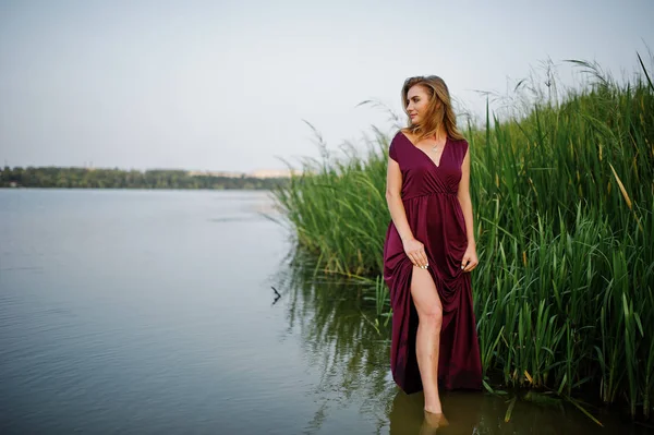 Blonde sensual woman in red marsala dress standing in water of l