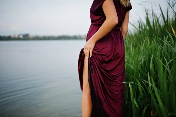 Blonde sensual woman in red marsala dress standing in water of l