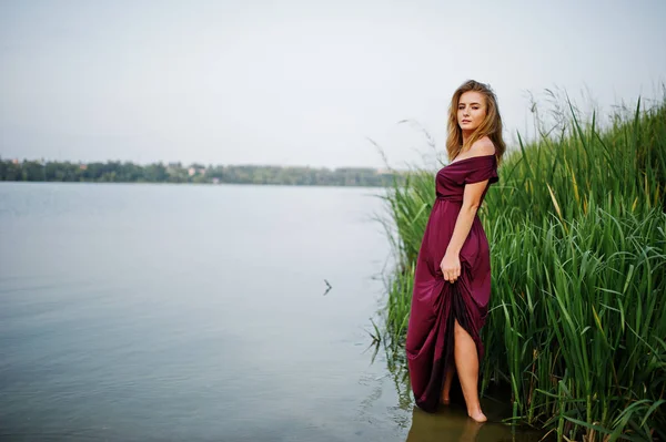 Loira sensual mulher em vermelho marsala vestido de pé na água de l — Fotografia de Stock