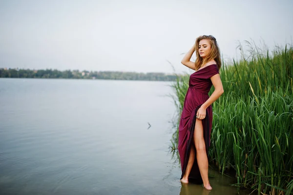 Blonde sensual woman in red marsala dress standing in water of l