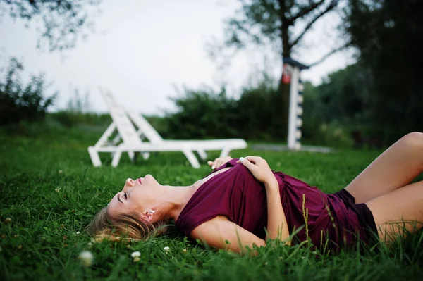 Блондинка чувственная женщина в красном платье марсала лежит в зеленой гра — стоковое фото