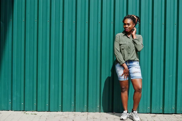 Mujer africana con rastas en el pelo, en pantalones cortos de jeans posados contra gr — Foto de Stock