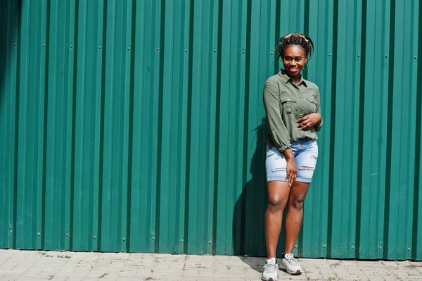 Mujer africana con rastas en el pelo, en pantalones cortos de jeans posados contra gr — Foto de Stock