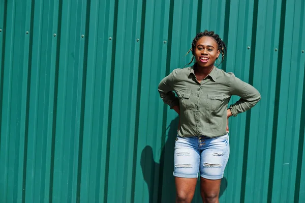 Mujer africana con rastas en el pelo, en pantalones cortos de jeans posados contra gr — Foto de Stock