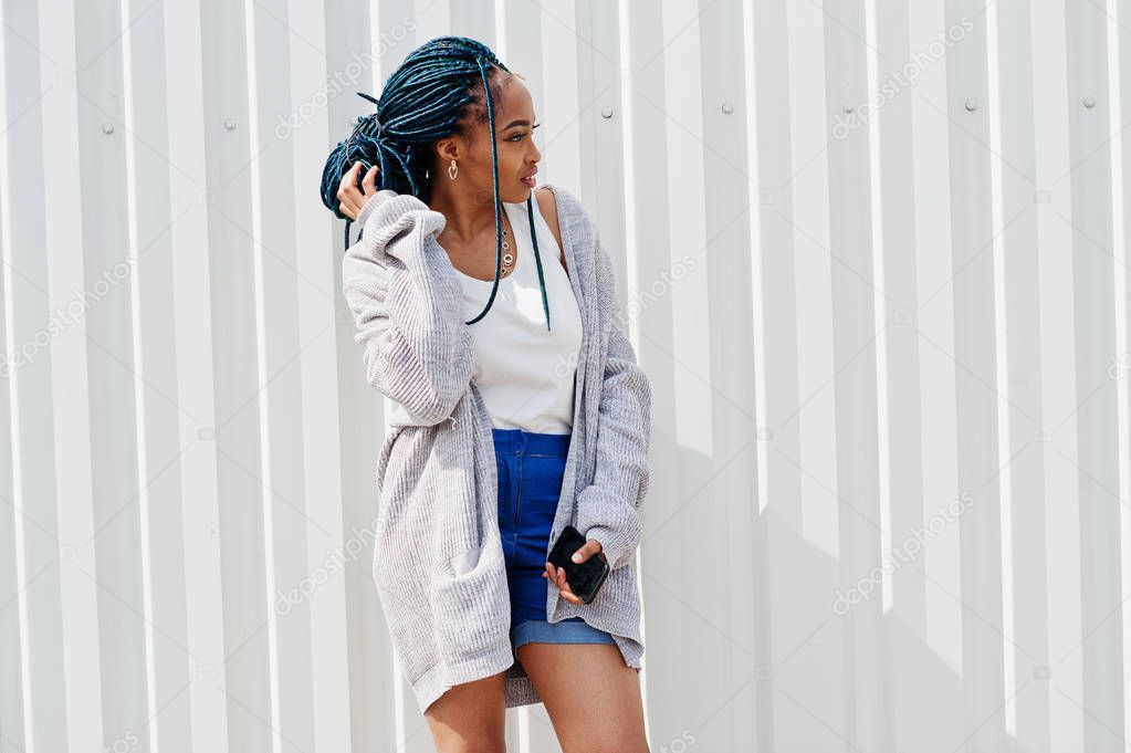 African woman with dreads hair, in jeans shorts  posed against w