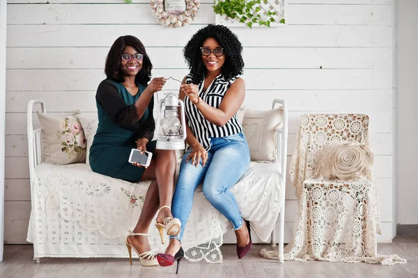 Duas amigas africanas usam óculos sentados no sofá em — Fotografia de Stock