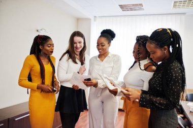 Beş çok ırklı iş kadını evraklarla ofiste duruyor 