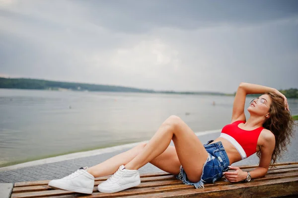 Sexy chica modelo rizado en top rojo, jeans pantalones cortos de mezclilla, gafas —  Fotos de Stock