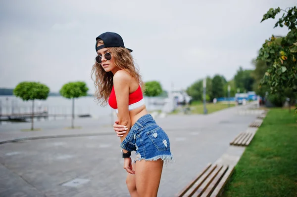 Menina modelo sexy em top vermelho, calça jeans denim shorts mostrar suas nádegas — Fotografia de Stock