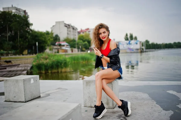 Sexy krullend model meisje in rode top, jeans denim shorts, lederen Ja — Stockfoto