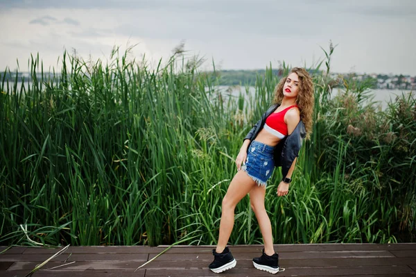 Сексуальна кучерява дівчина моделі в червоному верхньому кутку, джинсові джинсові шорти, шкіряна в'язниця — стокове фото