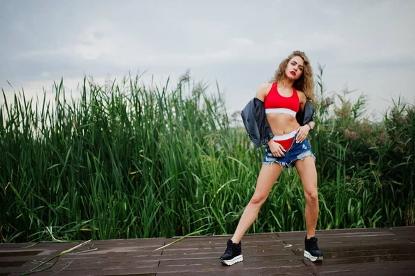 赤いトップ、ジーンズデニムショートパンツ、レザーjaのセクシーなカーリーモデルの女の子 — ストック写真