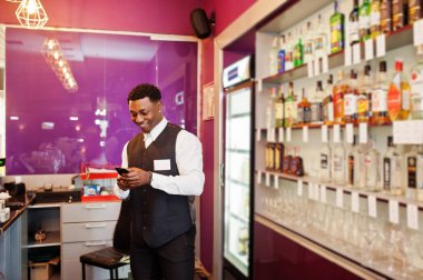 Elinde cep telefonu ile barda Afrikalı Amerikalı barmen.