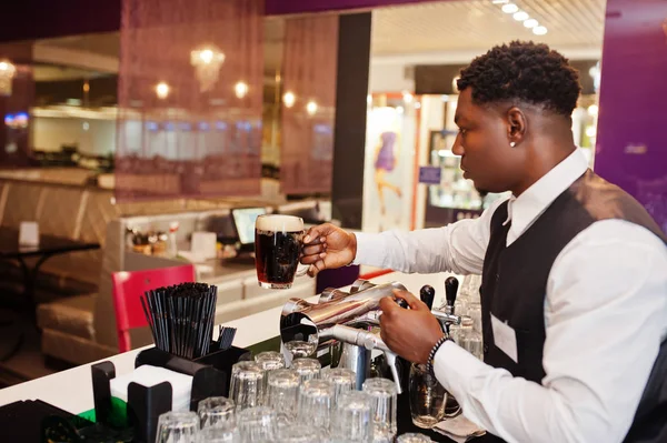 African american bartender at bar hold fresh dark beer at glass