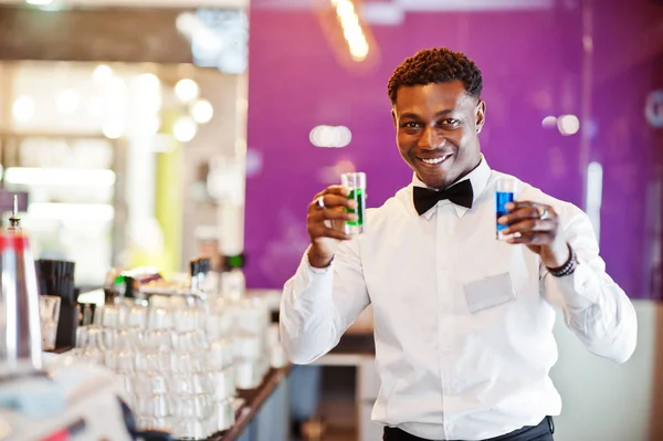 African american bartender at bar holding two coctail shots. Alc