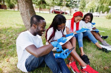 Group of happy african volunteers sitting under tree at park and clipart