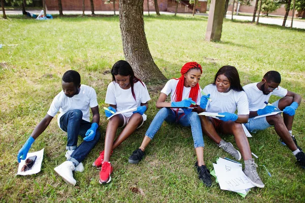 Gruppe fröhlicher afrikanischer Freiwilliger sitzt unter einem Baum im Park und — Stockfoto