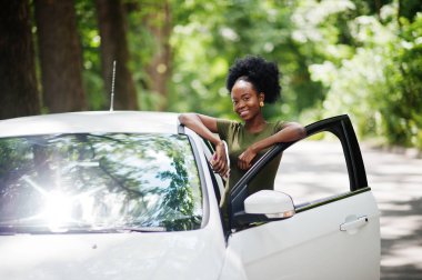 Afro-Amerikalı kadın orman yolunda beyaz otomobile karşı poz verdi.