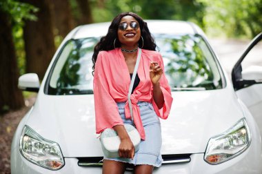 Afro-Amerikalı kadın orman yolunda beyaz otomobile karşı poz verdi.