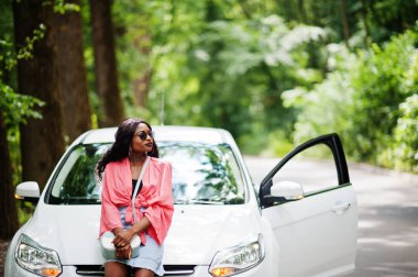 Afro-Amerikalı kadın orman yolunda beyaz otomobile karşı poz verdi.