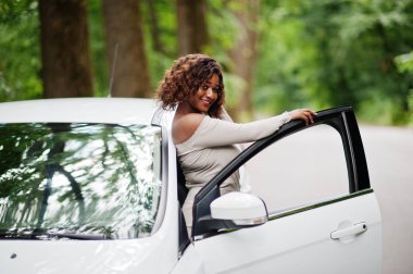 Afro-Amerikalı kadın orman yolunda beyaz otomobile karşı poz verdi.
