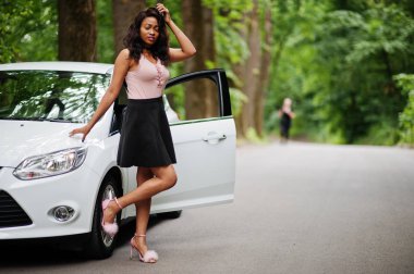 Afro-Amerikalı kadın orman yolunda beyaz otomobile karşı poz verdi.