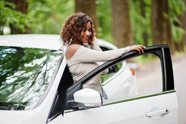 Афроамериканець жінка позувала проти білого автомобіля в лісовій дорозі. — стокове фото