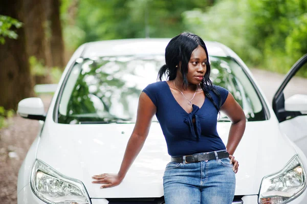 Афроамериканець жінка позувала проти білого автомобіля в лісовій дорозі. — стокове фото