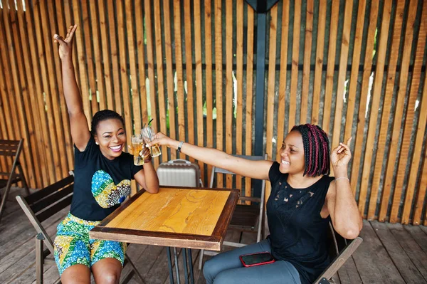 Two african american girls drinking and cheering together.
