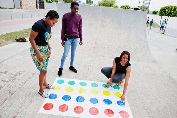 Group of three african american friends play twister game outdoo