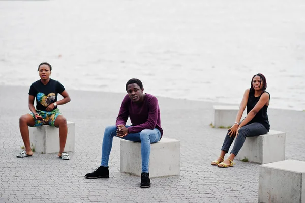 Tre afroamerikanska vänner sitter på stenkuber utomhus. — Stockfoto