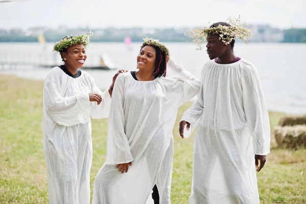 Three african american friends on white cloaks and wreath having