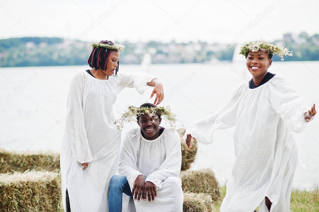 Three african american friends on white cloaks and wreath having