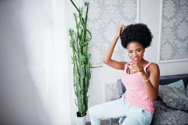 Ung afrikansk amerikansk kvinna i rosa linne sitter på hennes rum — Stockfoto