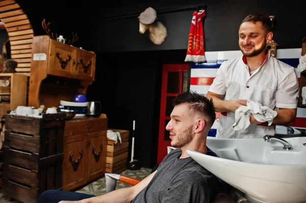 年轻的胡子男子洗头由理发师，而坐在c — 图库照片