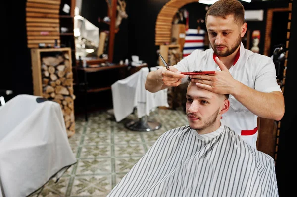 Young bearded man getting haircut by hairdresser while sitting i
