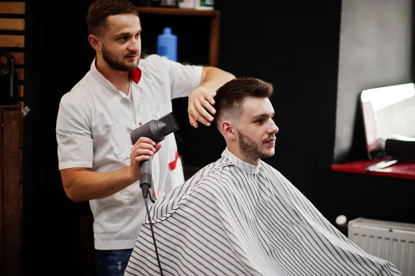 Young bearded man getting haircut by hairdresser while sitting i