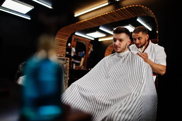 Jeune homme barbu se faire couper les cheveux par coiffeur tout en étant assis i — Photo